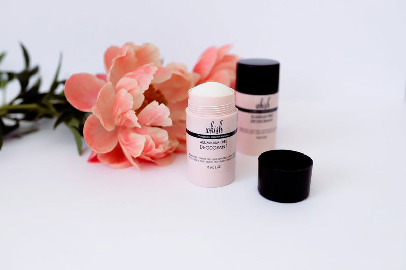 Two Whish Aluminum-Free Deodorant sticks beside a peach peony, styled for a clean, gentle body-care vibe.
