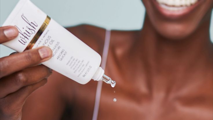 A woman dispenses drops of Whish Coconut Milk + Verbena Luminous Body Oil from a small tube.
