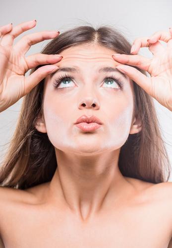 young brunette woman touching forehead wrinkles 