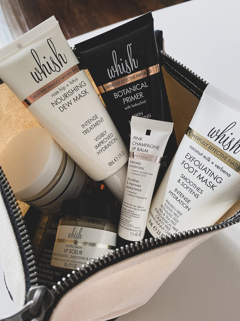Travel bag filled with Whish natural skincare products including face masks, lip balm, botanical primer, and scrubs.
